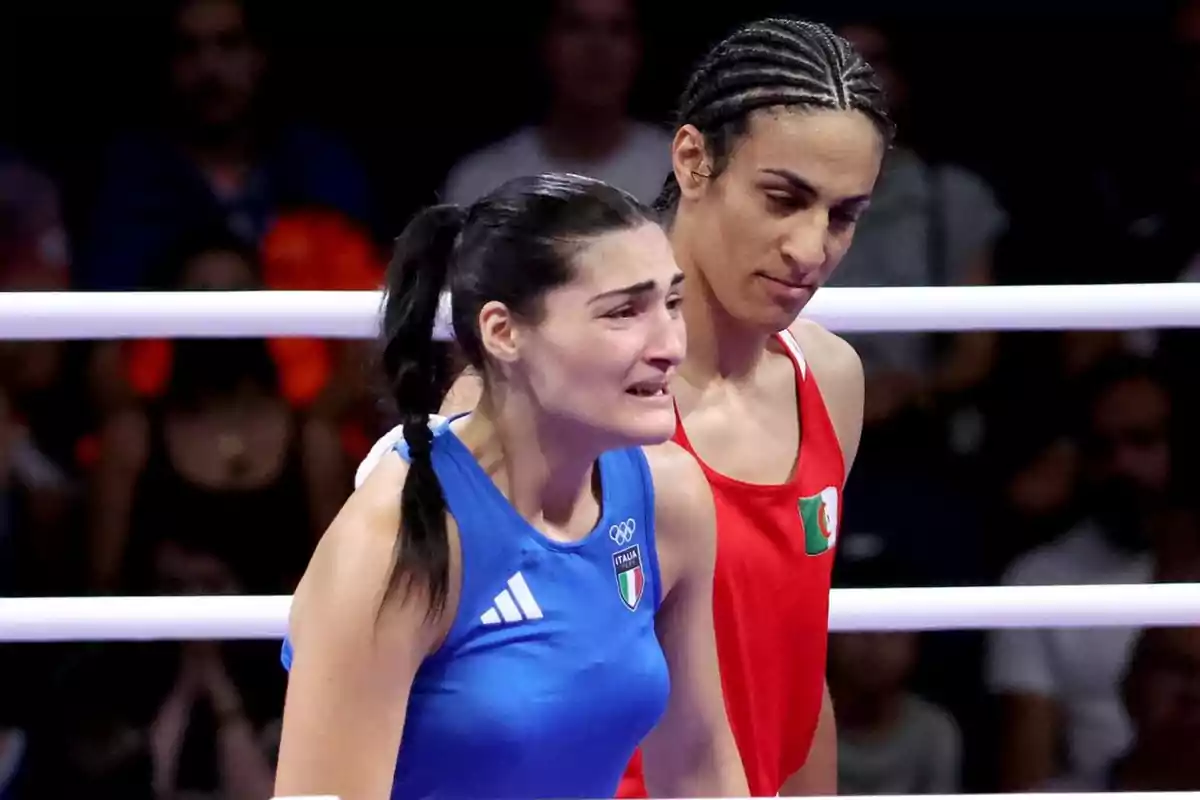 Dos boxeadoras en el ring, una con uniforme azul y otra con uniforme rojo, en un momento emotivo después de un combate.