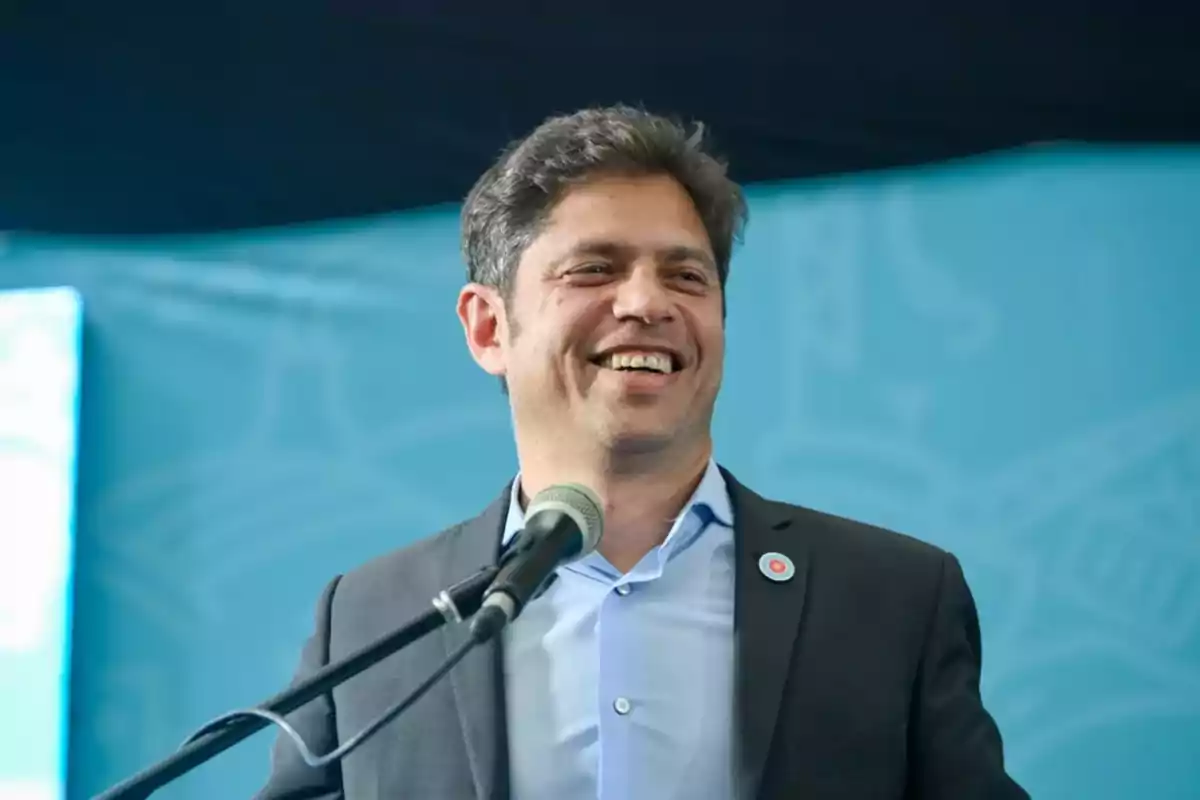 A smiling man speaking in front of a microphone with a blue background.