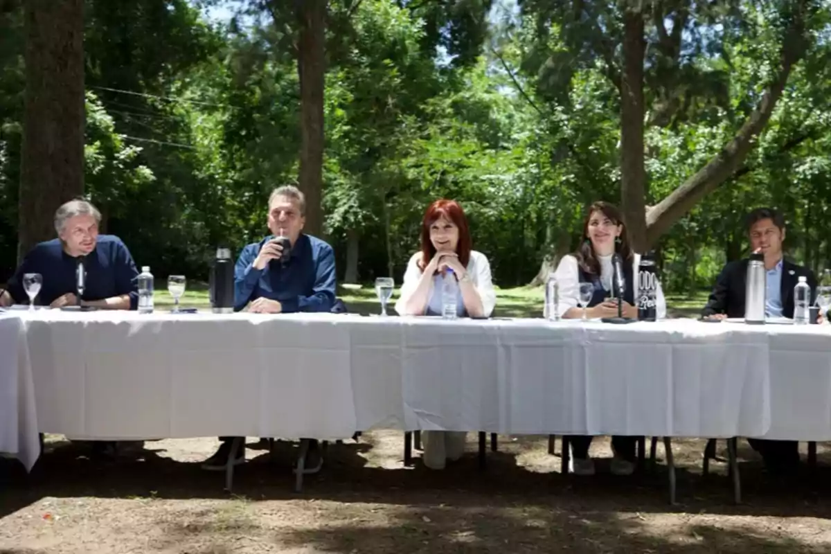 Un grupo de personas sentadas en una mesa larga al aire libre rodeados de árboles.