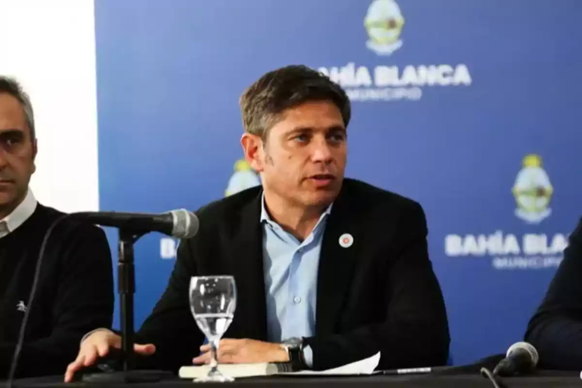 Un hombre hablando en una conferencia de prensa con un micrófono frente a él y un fondo azul que dice "Bahía Blanca Municipio".