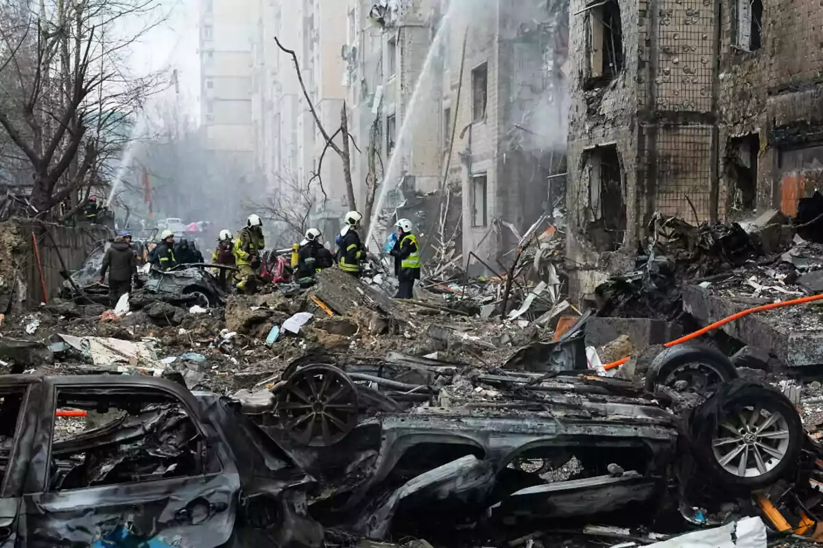 Bomberos trabajan entre los escombros y autos destruidos tras un ataque que dañó gravemente un edificio residencial