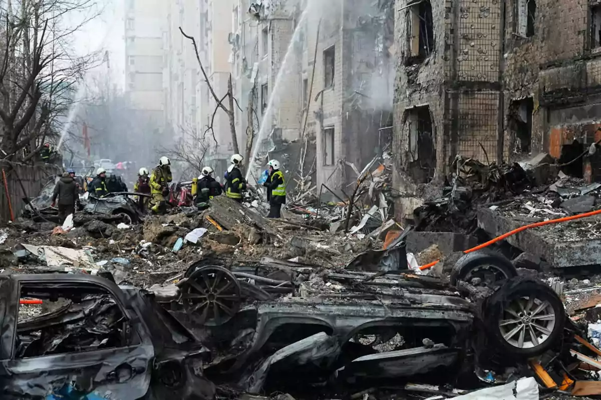 Firefighters work among the rubble of a damaged building, surrounded by destroyed vehicles and remnants of collapsed structures. Firefighters work among the rubble of a damaged building, surrounded by destroyed vehicles and remnants of collapsed structures.