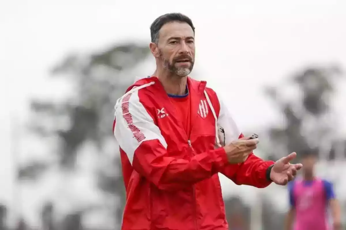 Entrenador de fútbol con chaqueta roja dando indicaciones en un campo al aire libre Entrenador de fútbol con chaqueta roja dando indicaciones en un campo al aire libre