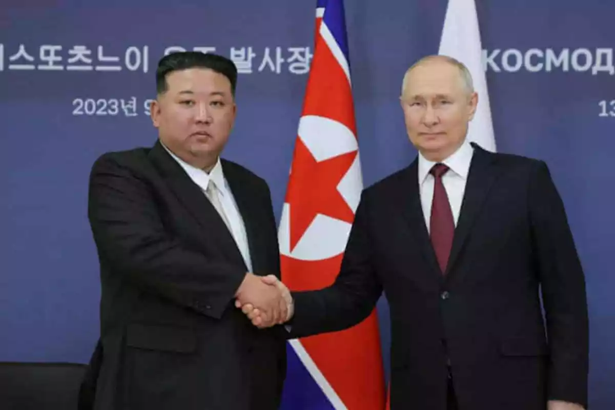 Two men in dark suits shake hands in front of flags and a blue background with text in Korean and Russian. Two men in dark suits shake hands in front of flags and a blue background with text in Korean and Russian.