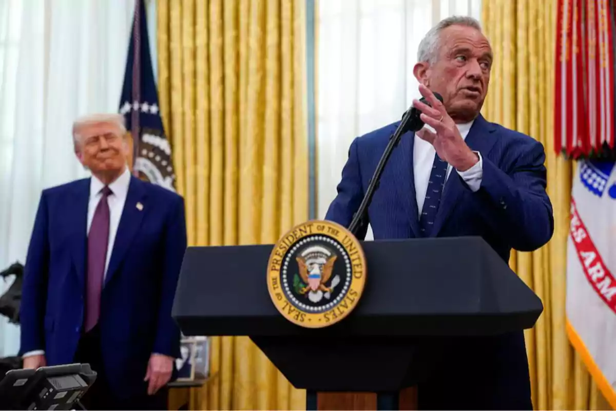 Two men at an official event in a room with golden curtains and a podium with the presidential seal.