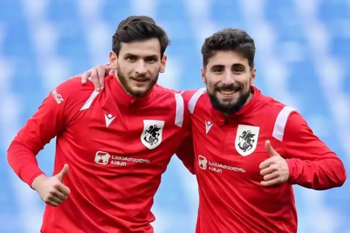 Dos futbolistas con uniforme rojo posan sonrientes en un estadio mostrando el pulgar arriba Dos futbolistas con uniforme rojo posan sonrientes en un estadio mostrando el pulgar arriba