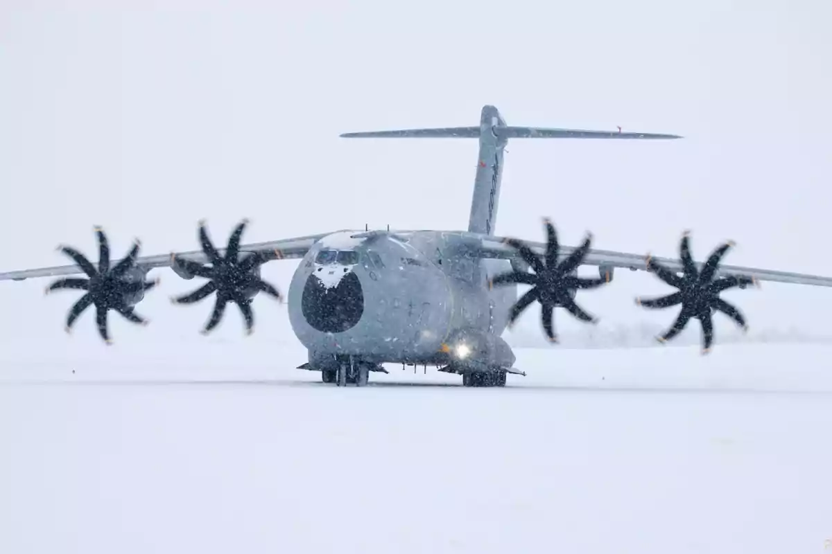 Un avión de transporte militar en una pista cubierta de nieve con hélices en movimiento.