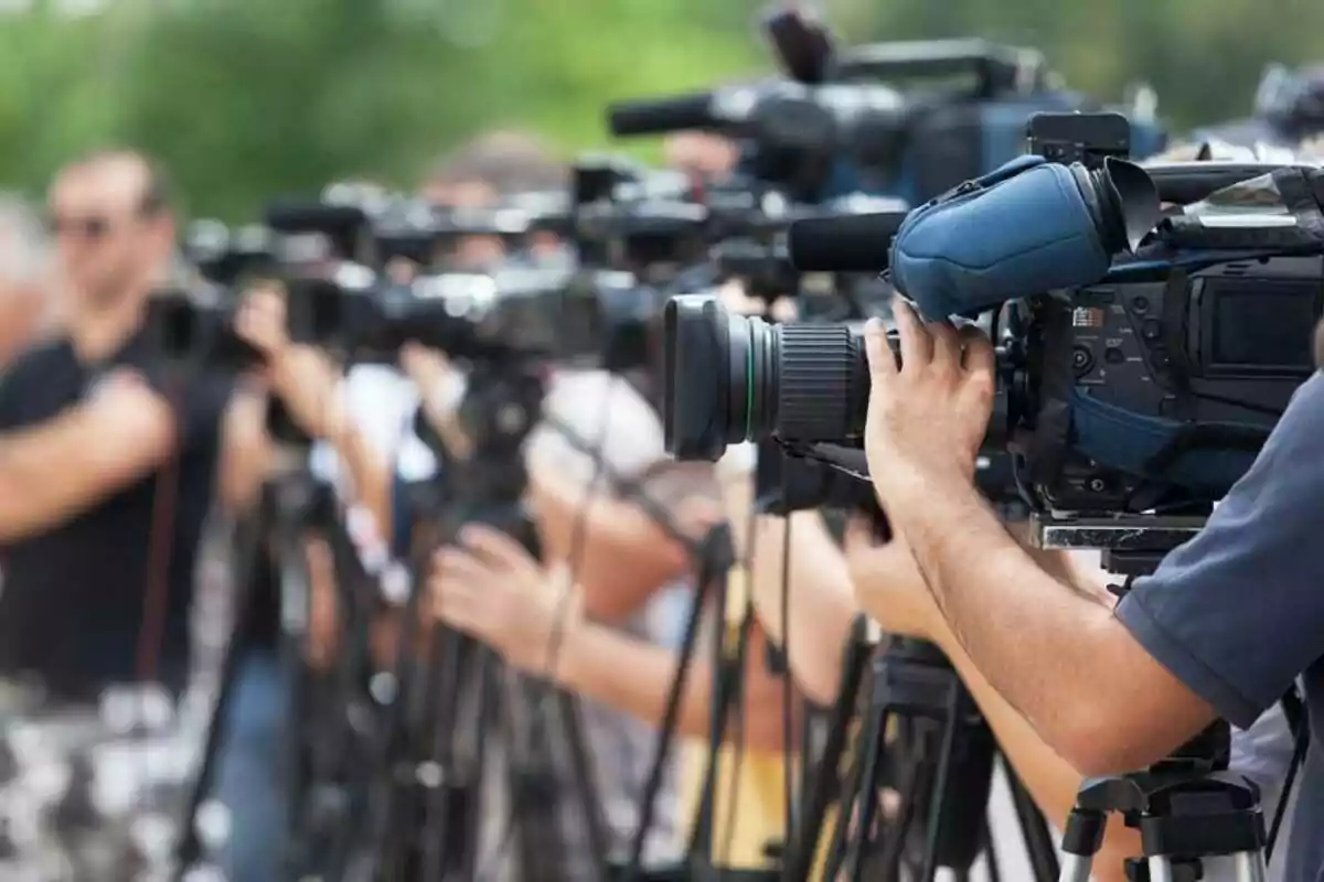 People operating video cameras at an outdoor event.