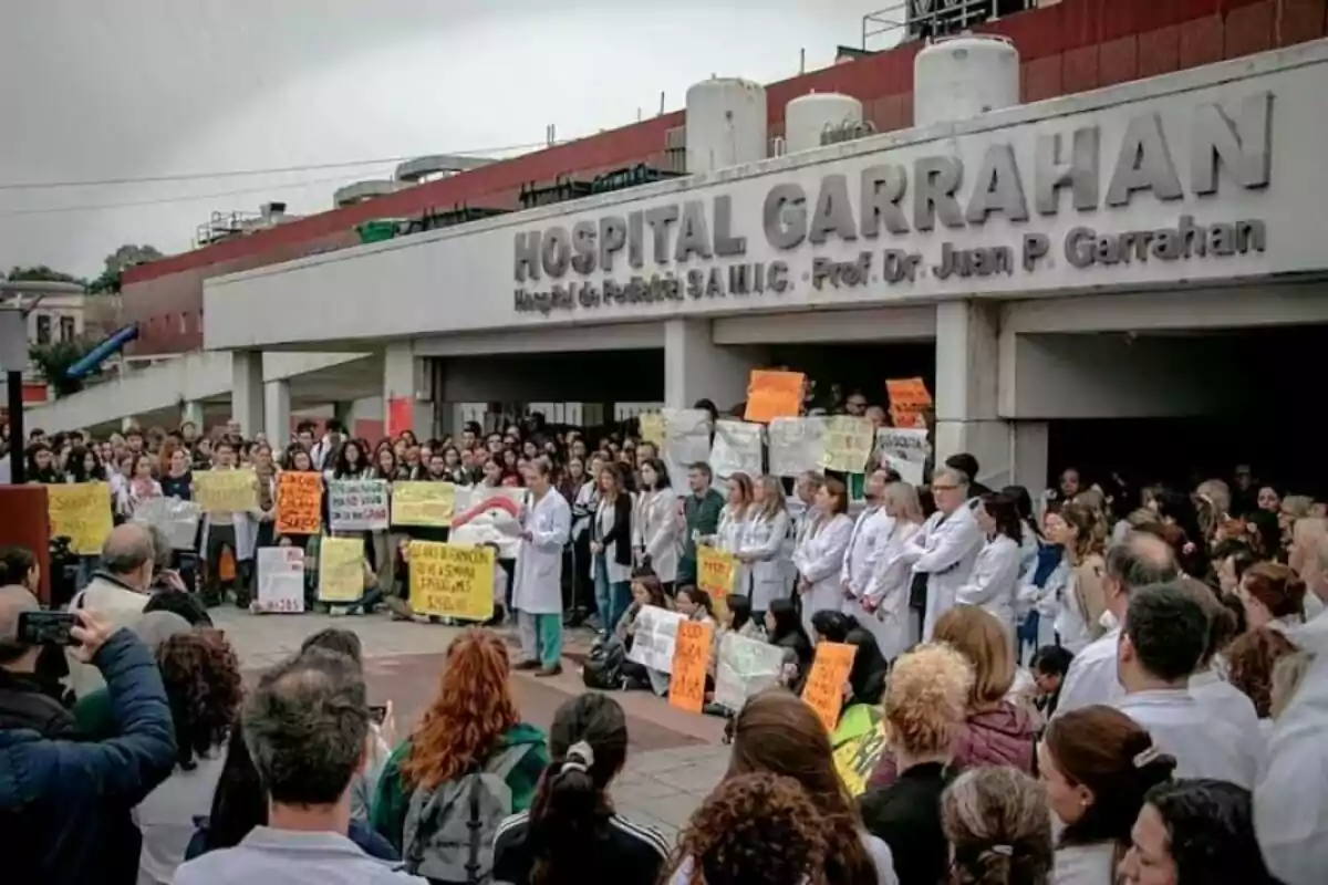 A large group of people, many wearing white lab coats, are protesting with signs in front of the entrance to Garrahan Hospital.