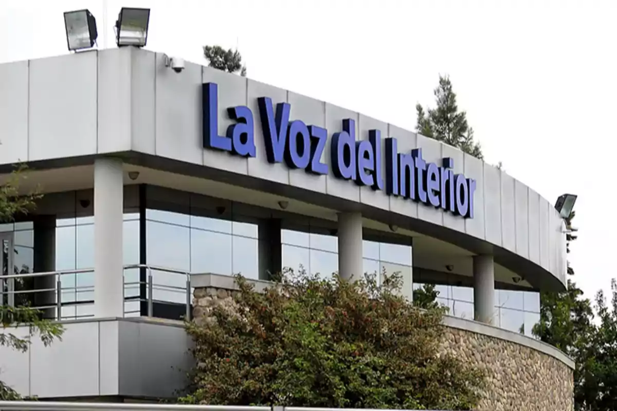 Edificio moderno con el cartel de La Voz del Interior en letras azules y grandes, rodeado de árboles y vegetación. Edificio moderno con el cartel de La Voz del Interior en letras azules y grandes, rodeado de árboles y vegetación.