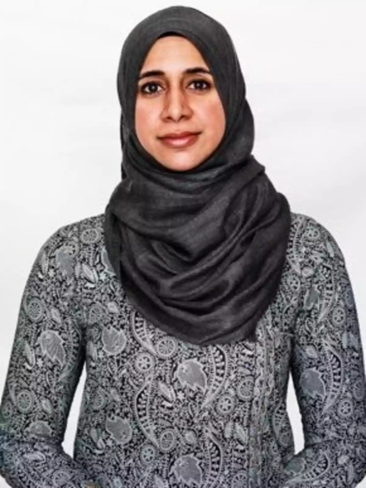 Una mujer con un hiyab gris y una blusa de patrón floral gris posando frente a un fondo blanco.