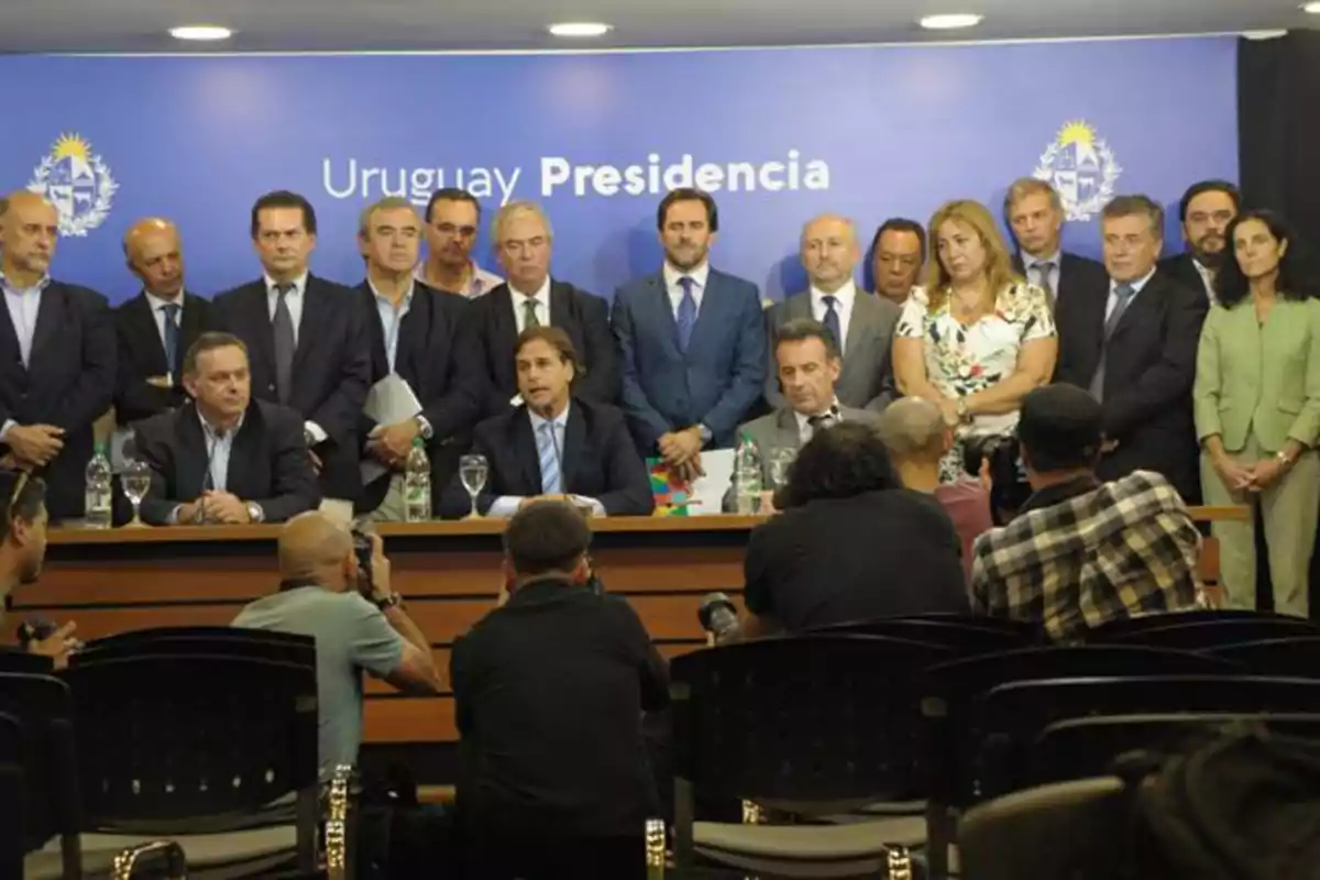 A group of people at a press conference in a room with a blue background that says A group of people at a press conference in a room with a blue background that says