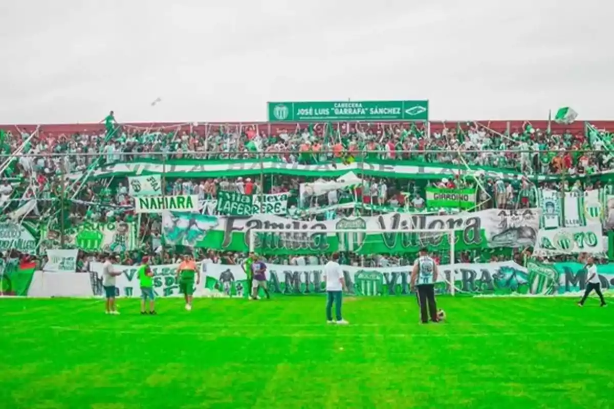 Aficionados de un equipo de fútbol en las gradas del estadio, con banderas y pancartas verdes y blancas.