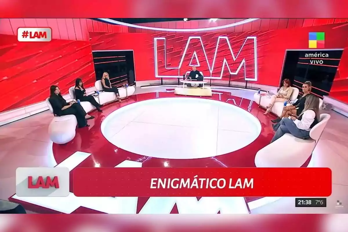 LAM TV set with several people sitting on white couches around a central table and a large red screen in the background displaying the show's logo LAM TV set with several people sitting on white couches around a central table and a large red screen in the background displaying the show's logo