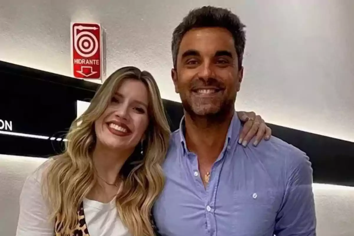 Una mujer y un hombre sonríen mientras posan juntos en un interior iluminado. Una mujer y un hombre sonríen mientras posan juntos en un interior iluminado.