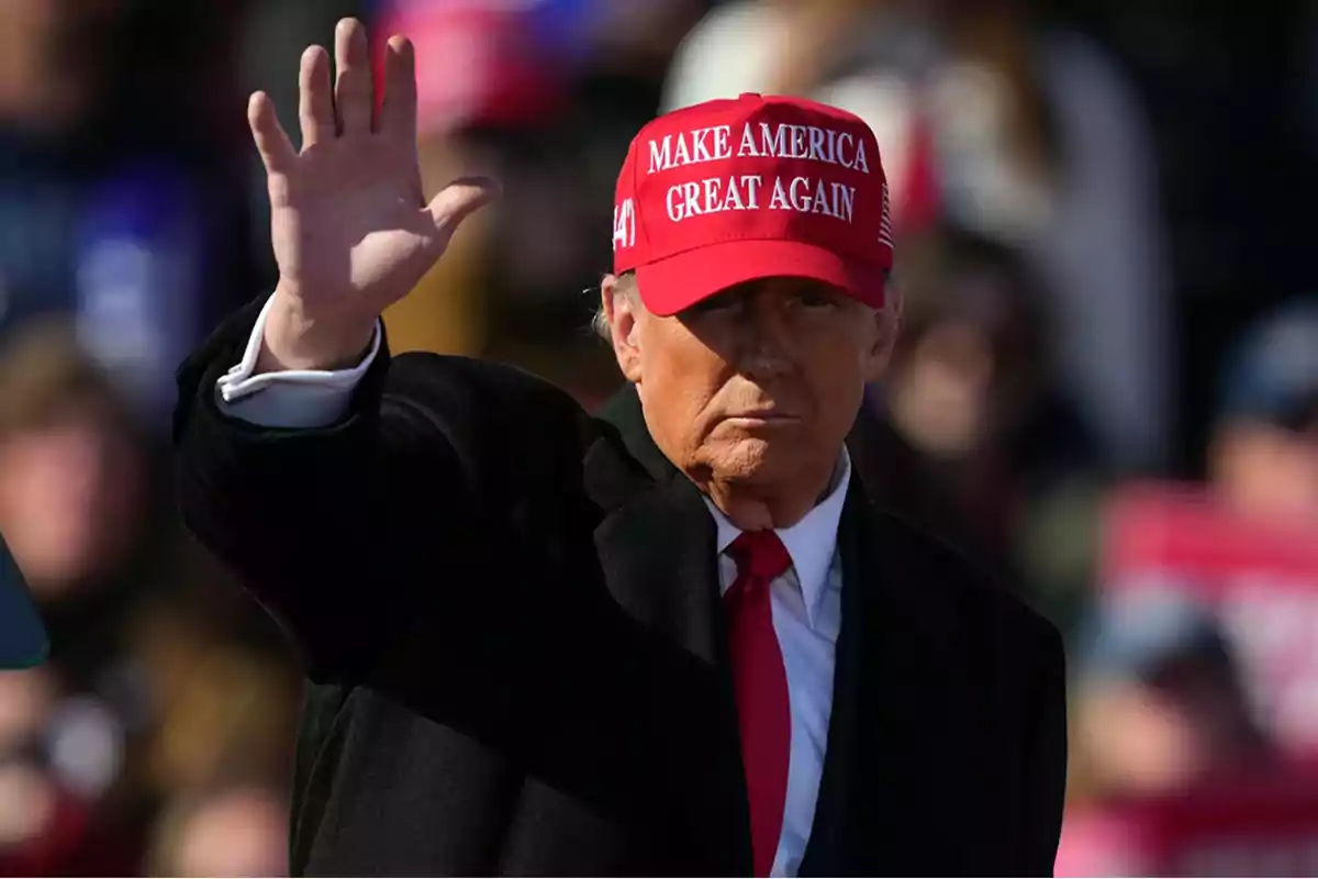 Persona con gorra roja que dice "Make America Great Again" levantando la mano.