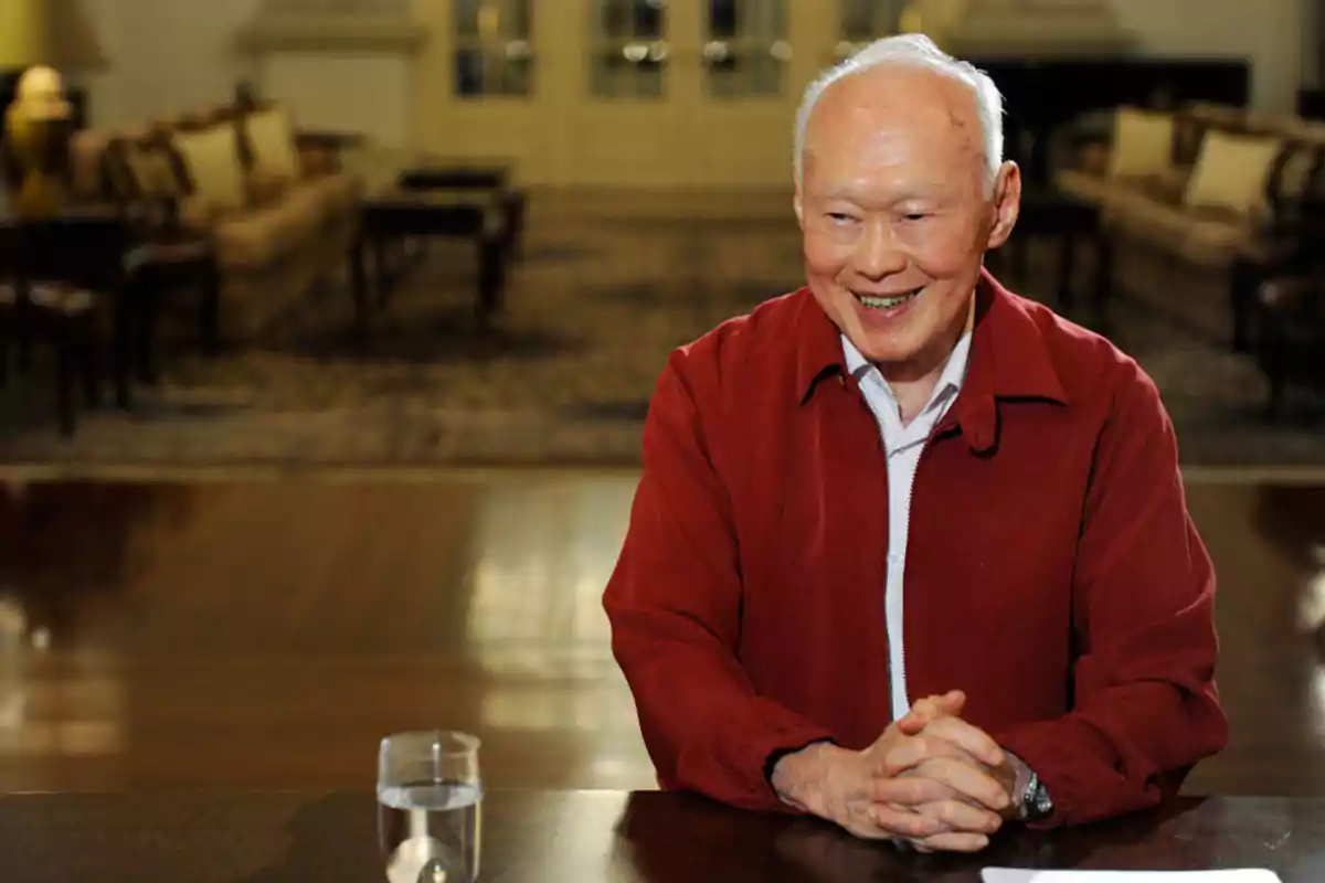 An elderly man smiles while sitting at a table with a glass of water in an elegant and cozy setting. An elderly man smiles while sitting at a table with a glass of water in an elegant and cozy setting.