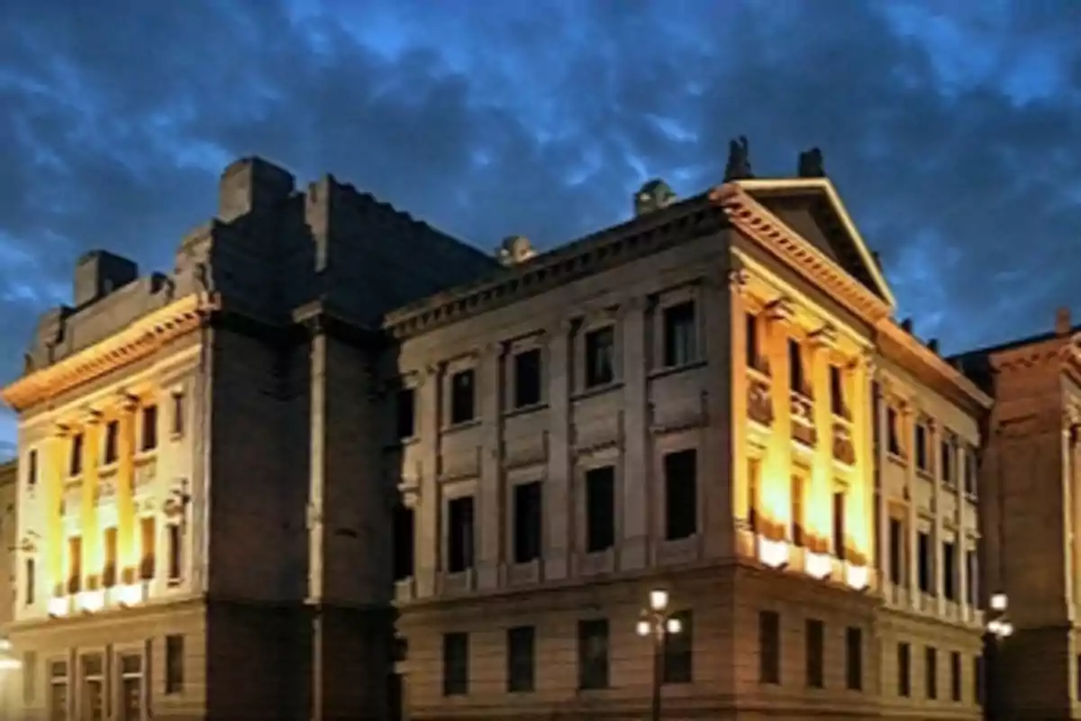 Un edificio histórico iluminado por la noche con un cielo nublado de fondo.