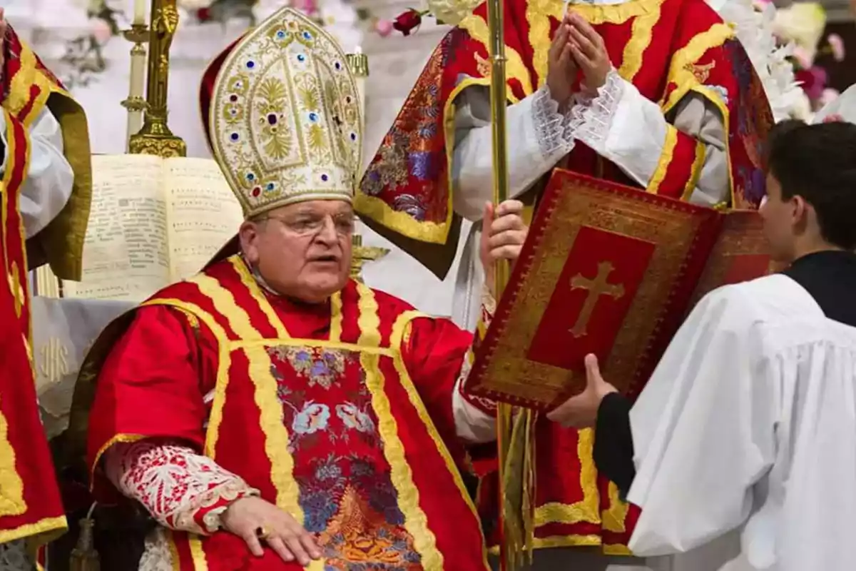 Un clérigo con vestimenta ceremonial roja y dorada sostiene un báculo mientras un asistente le presenta un libro religioso en una ceremonia. Un clérigo con vestimenta ceremonial roja y dorada sostiene un báculo mientras un asistente le presenta un libro religioso en una ceremonia.
