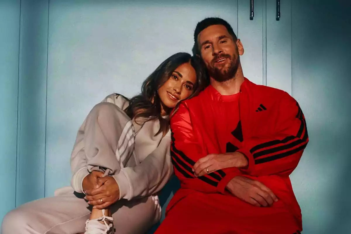 Dos personas sentadas juntas en un ambiente iluminado, una de ellas lleva un conjunto deportivo rojo y la otra un conjunto deportivo claro.