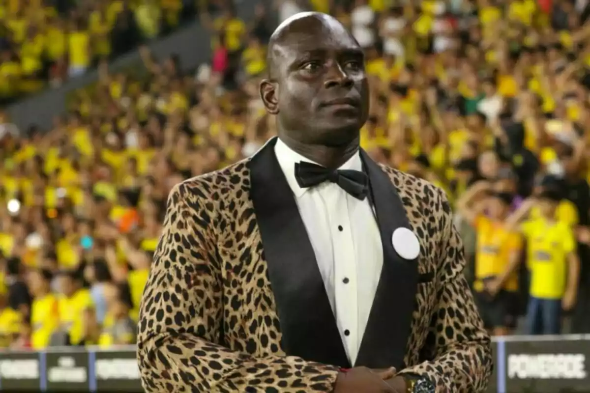 Man standing in an animal print tuxedo and black bow tie in a stadium full of people dressed in yellow