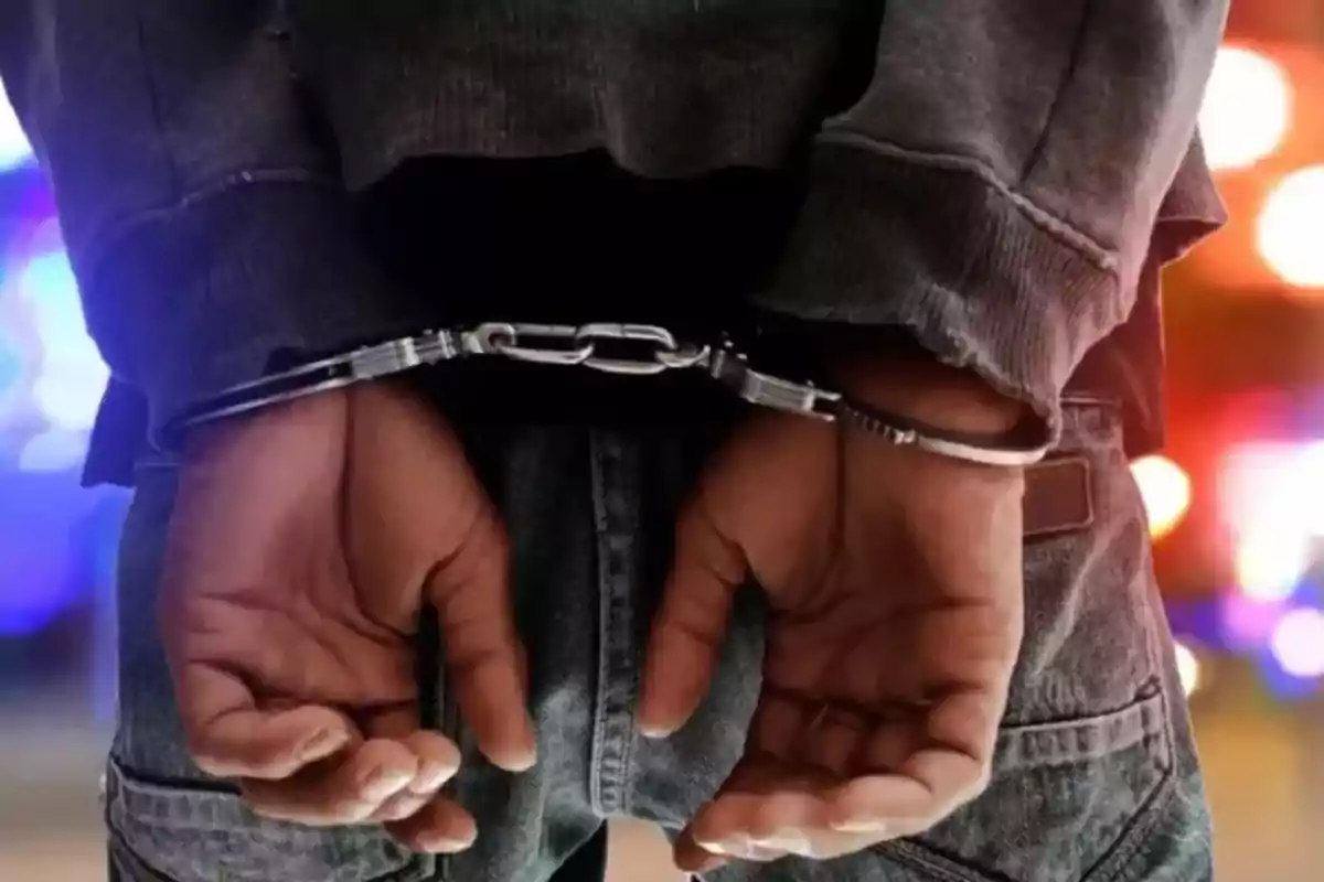 Person with hands handcuffed behind their back, with blurred lights in the background.