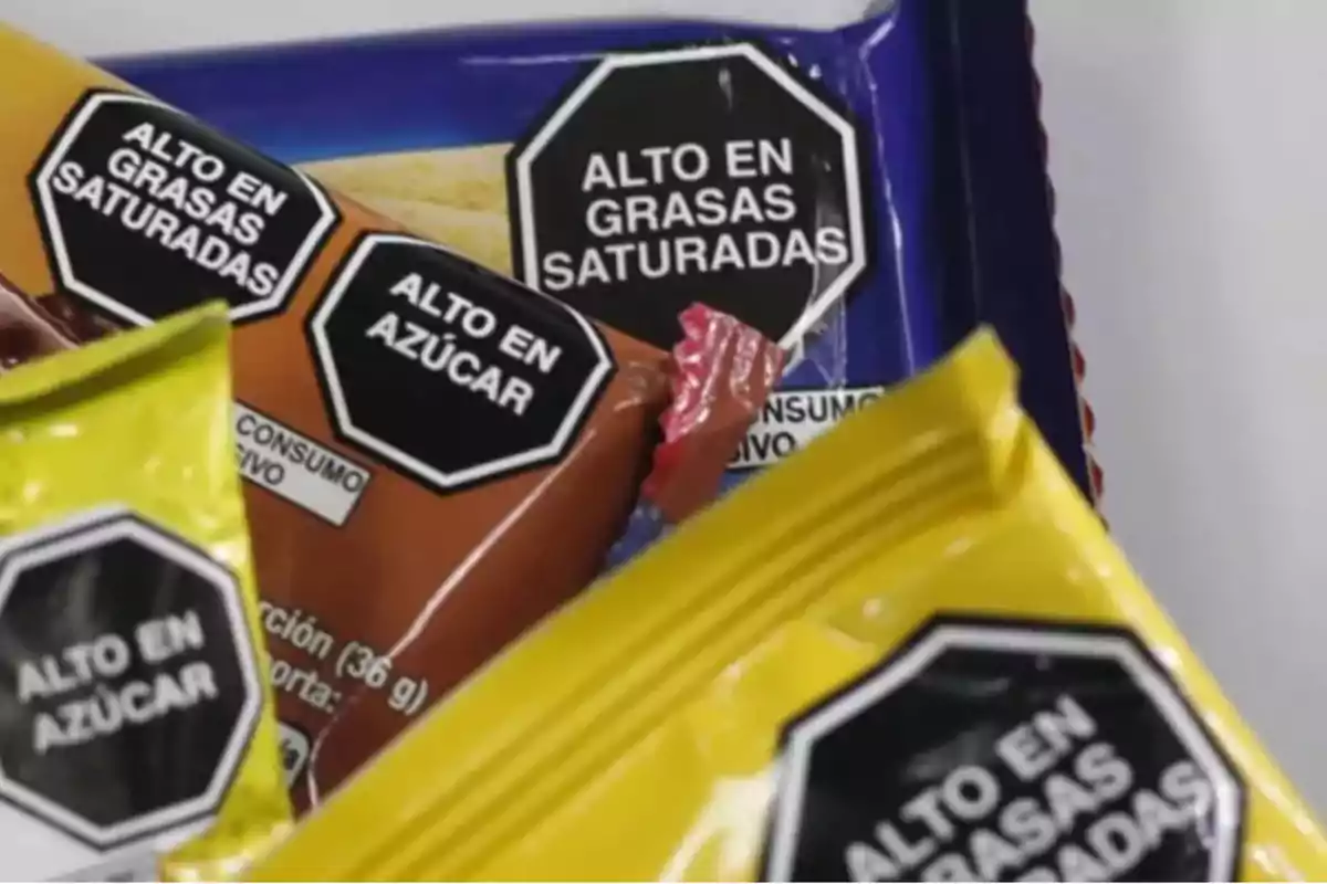 Paquetes de alimentos con etiquetas de advertencia que indican alto contenido en grasas saturadas y azúcar.