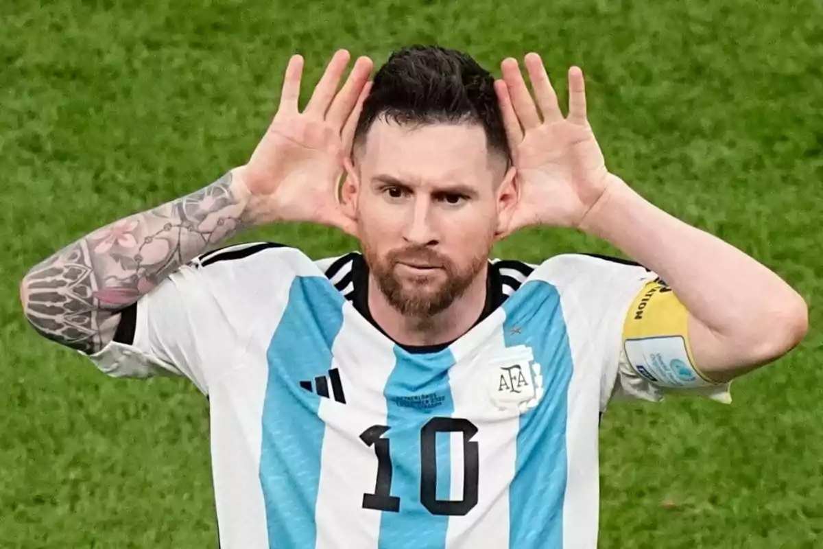 Jugador de fútbol con la camiseta de Argentina celebrando con las manos detrás de las orejas.