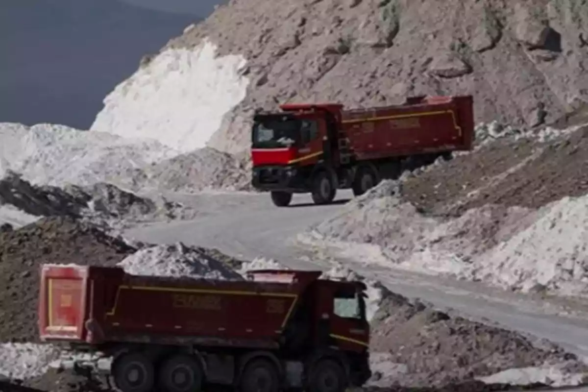 Dos camiones rojos transportan material en un camino rodeado de montañas de tierra y rocas.