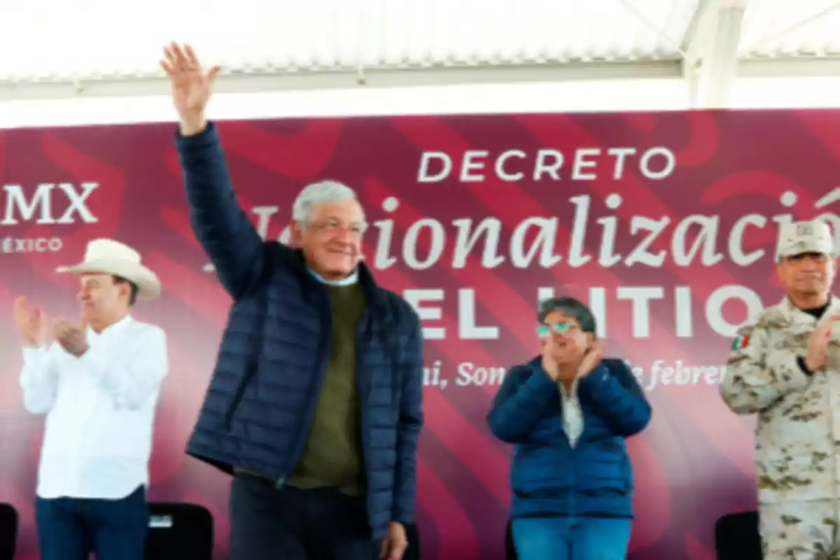 Un grupo de personas en un evento público con un hombre levantando la mano frente a un cartel que dice "Decreto Nacionalización".