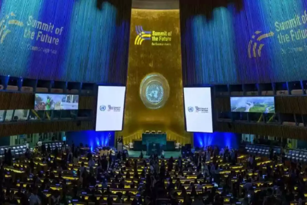 Una conferencia internacional en un auditorio grande con pantallas y proyecciones iluminadas en azul y dorado.