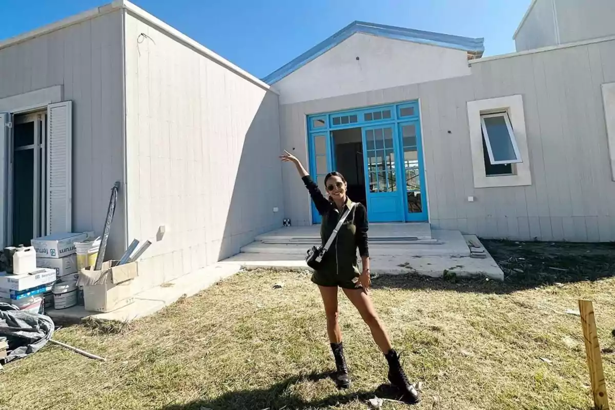 Persona posando frente a una casa en construcción con puerta azul y cielo despejado. Persona posando frente a una casa en construcción con puerta azul y cielo despejado.