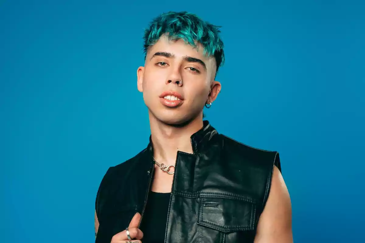 Joven con cabello teñido de azul, usando chaleco de cuero negro y fondo azul Joven con cabello teñido de azul, usando chaleco de cuero negro y fondo azul