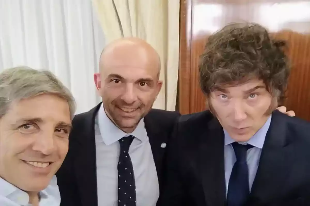 Three men pose together for a photo, all wearing formal suits and smiling.