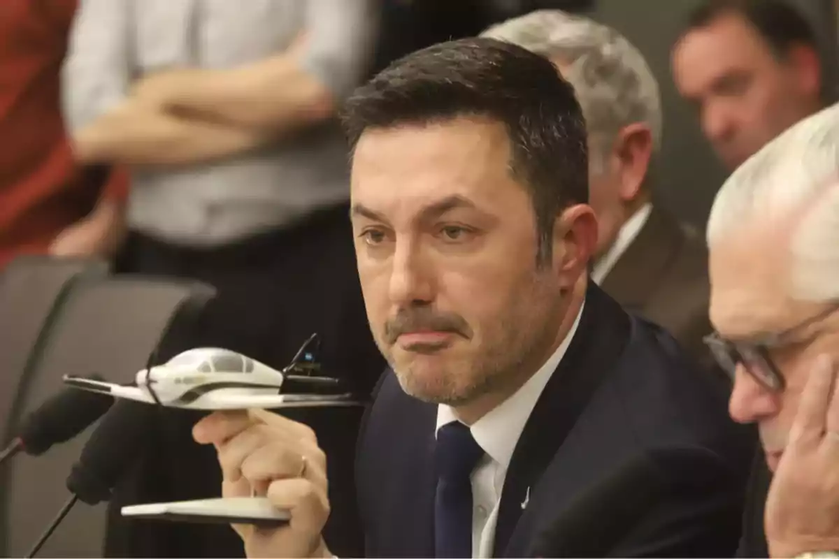 Man in a suit holding a model airplane during a meeting or conference
