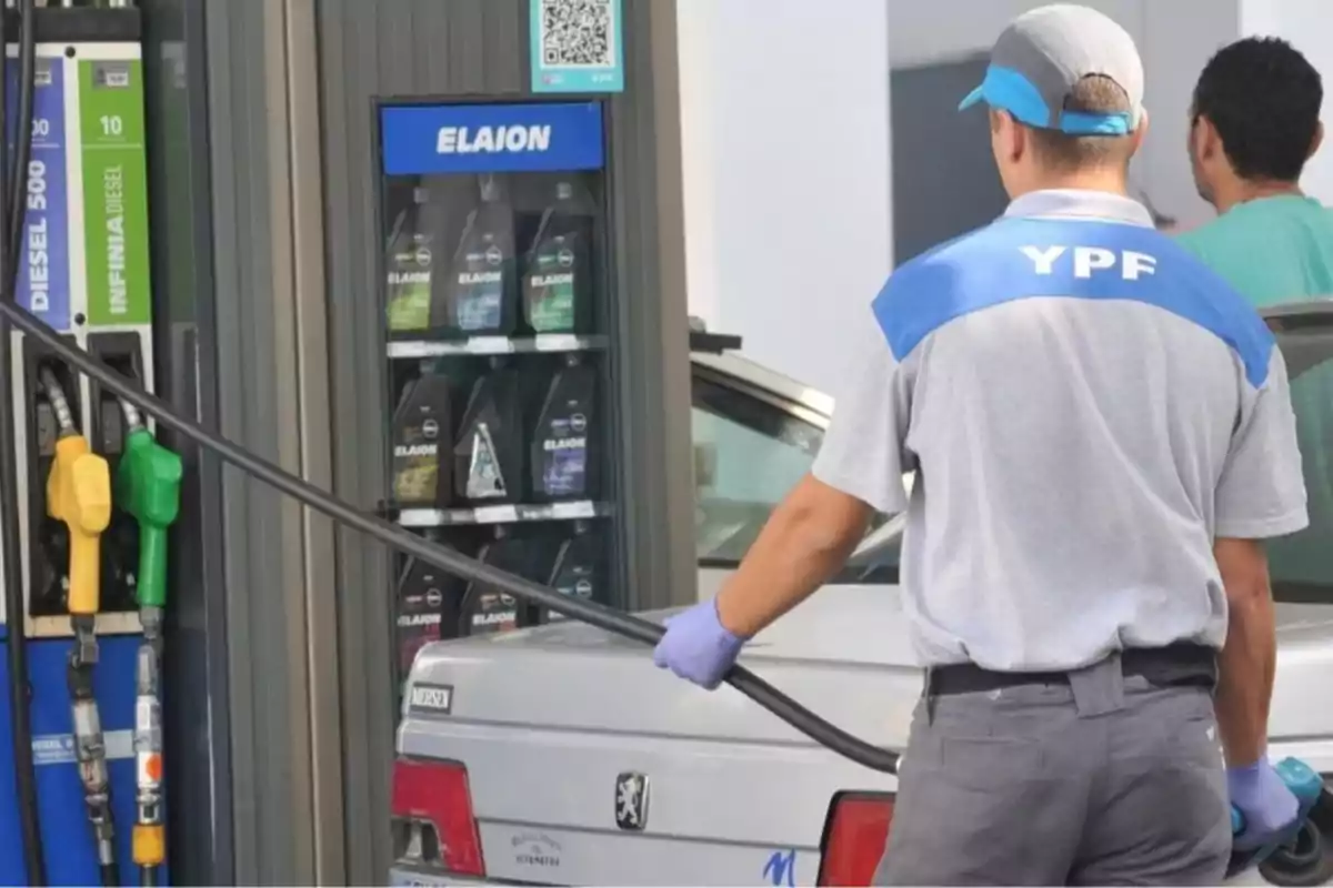 Un trabajador de estación de servicio con uniforme de YPF está llenando el tanque de un automóvil en una gasolinera.