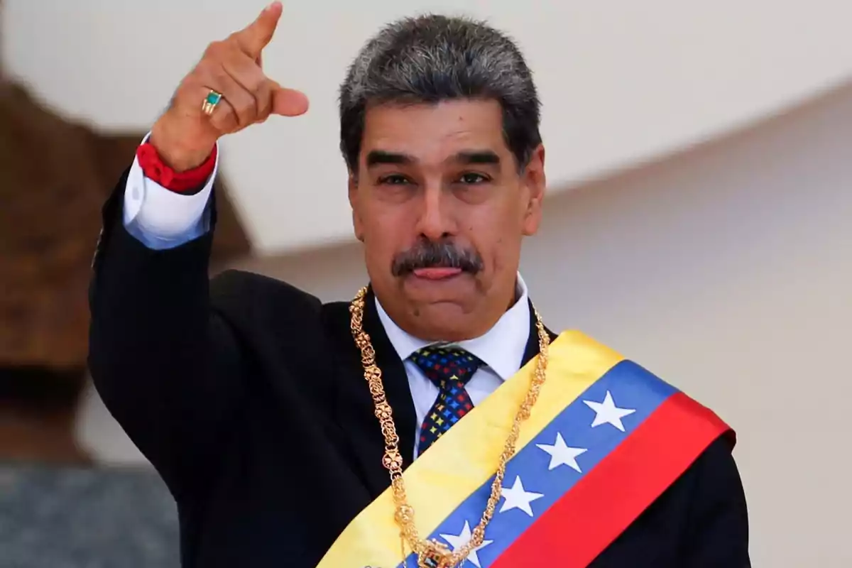 Man with a mustache wearing the Venezuelan presidential sash and a gold chain, raising his hand and pointing forward
