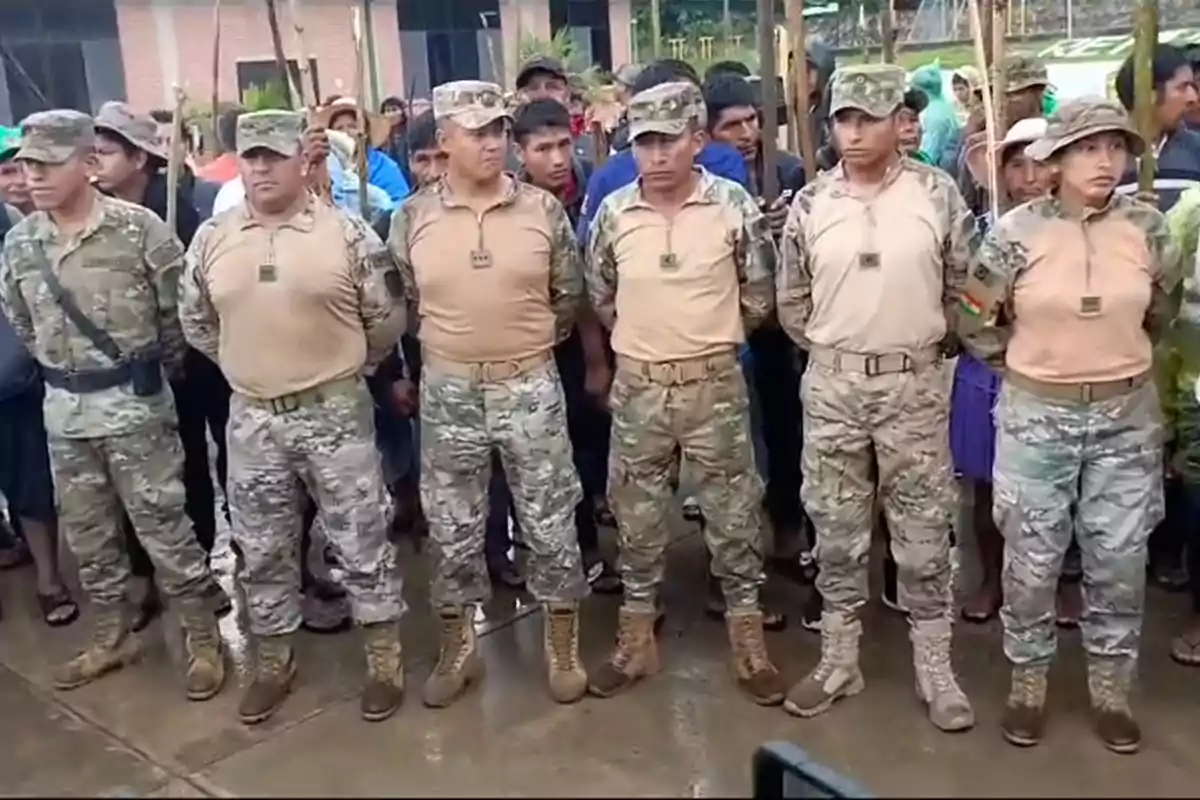 Un grupo de personas vestidas con uniformes militares camuflados está de pie en formación frente a una multitud.