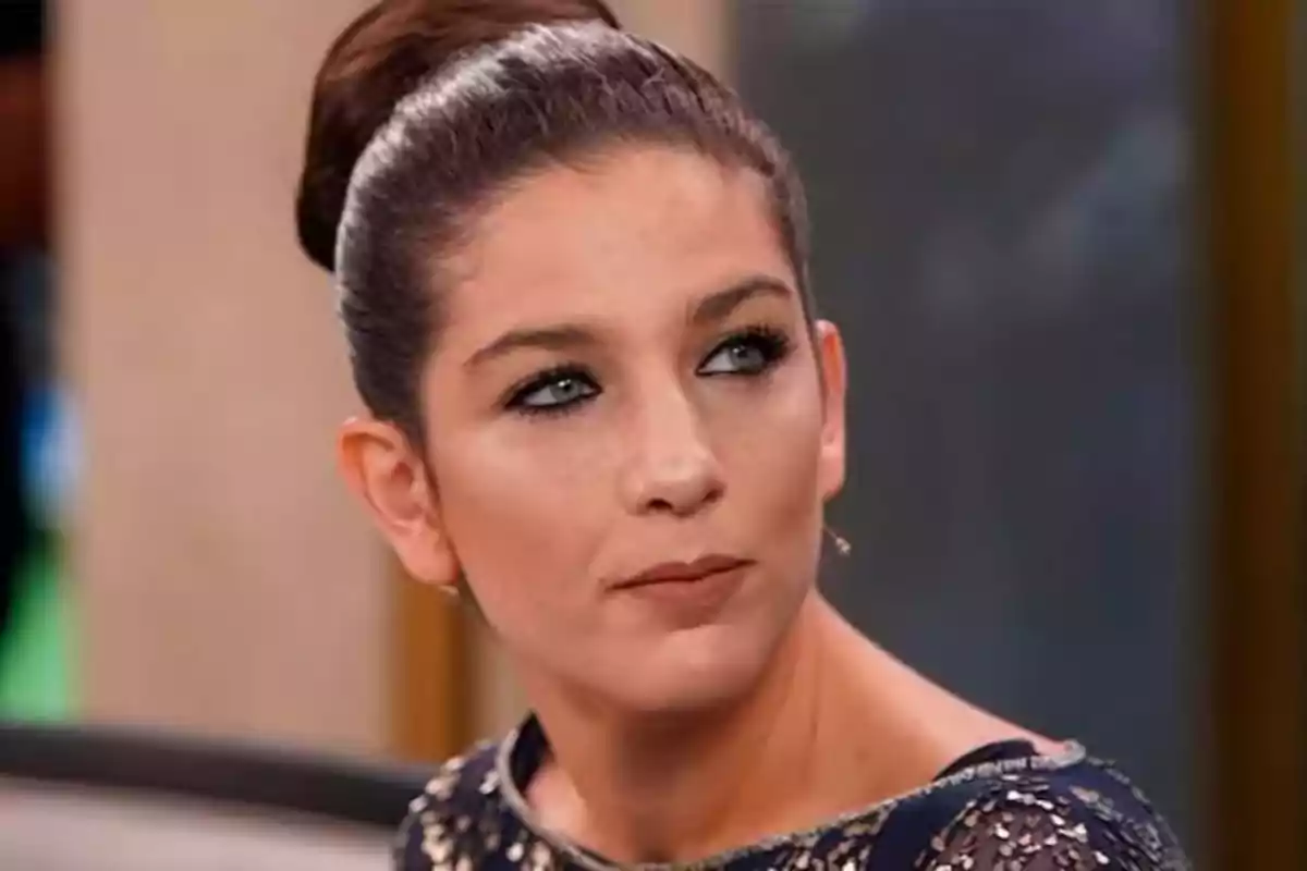 Una persona con cabello recogido y maquillaje elegante mira hacia un lado en un entorno interior. Una persona con cabello recogido y maquillaje elegante mira hacia un lado en un entorno interior.