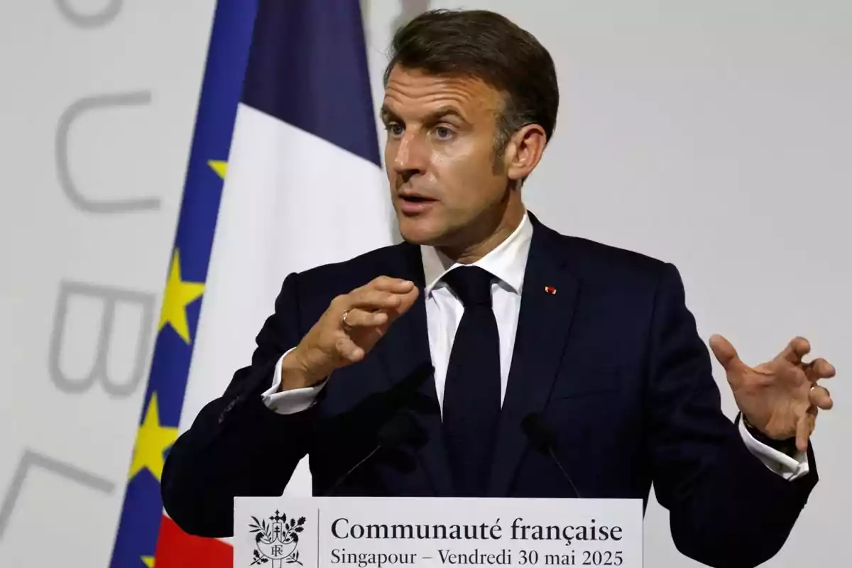 Hombre de traje oscuro hablando en un podio con banderas de Francia y la Unión Europea de fondo
