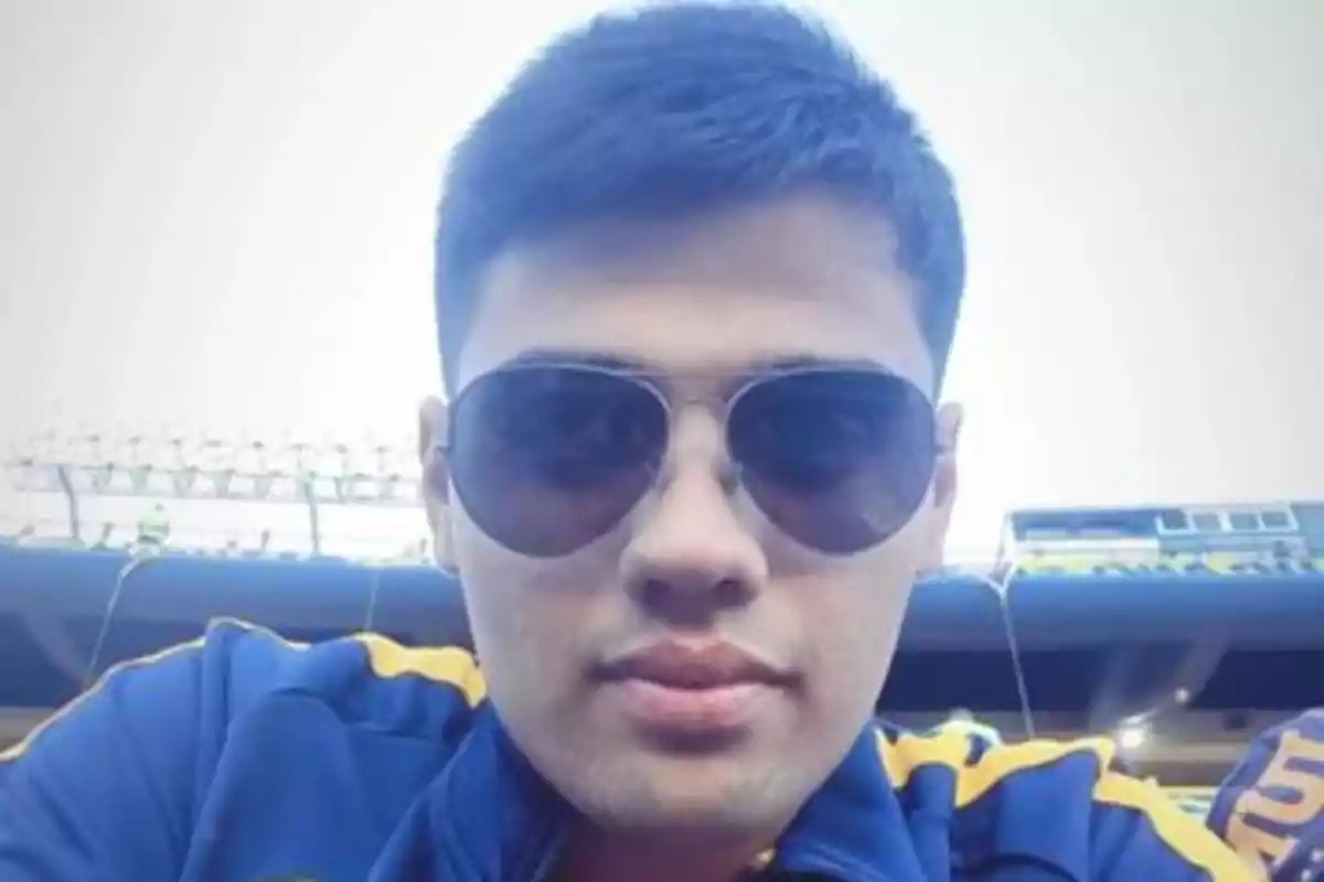 Un hombre con gafas de sol y chaqueta deportiva en un estadio.