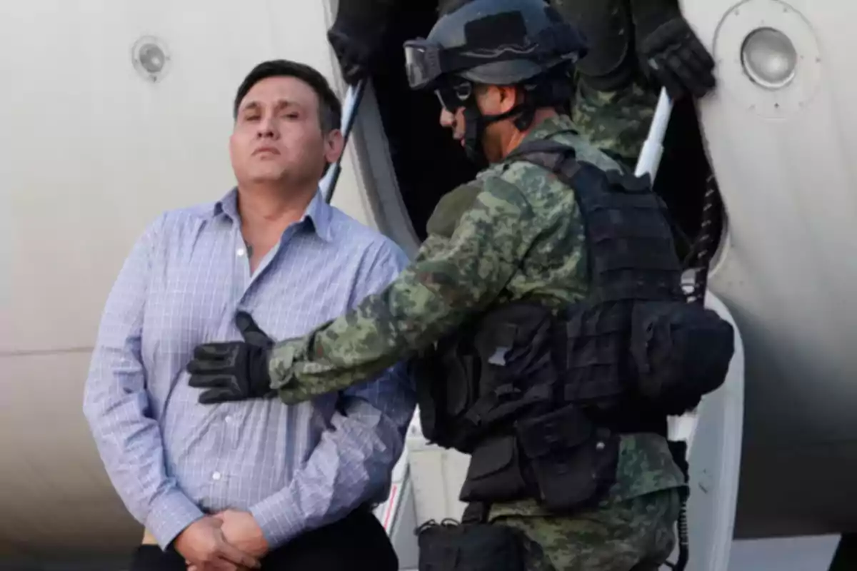 Un hombre con uniforme militar escolta a otro hombre esposado frente a un avión.