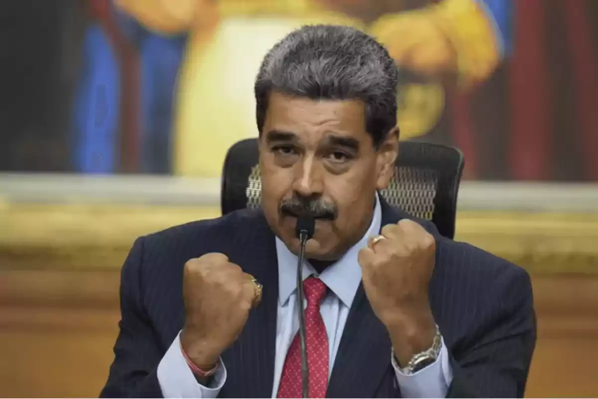 Un hombre con traje y corbata roja, con los puños levantados, hablando frente a un micrófono.