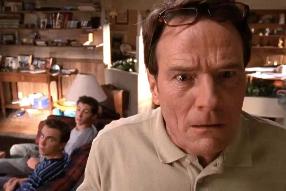 A man with a surprised expression is in the foreground while two young people watch him from a couch in a messy family room. A man with a surprised expression is in the foreground while two young people watch him from a couch in a messy family room.