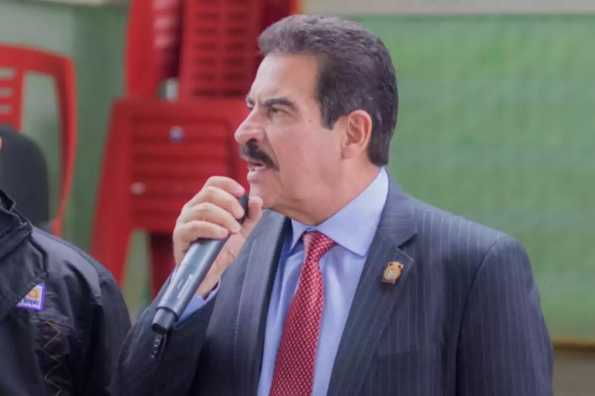 Un hombre con traje y corbata roja hablando por un micrófono.