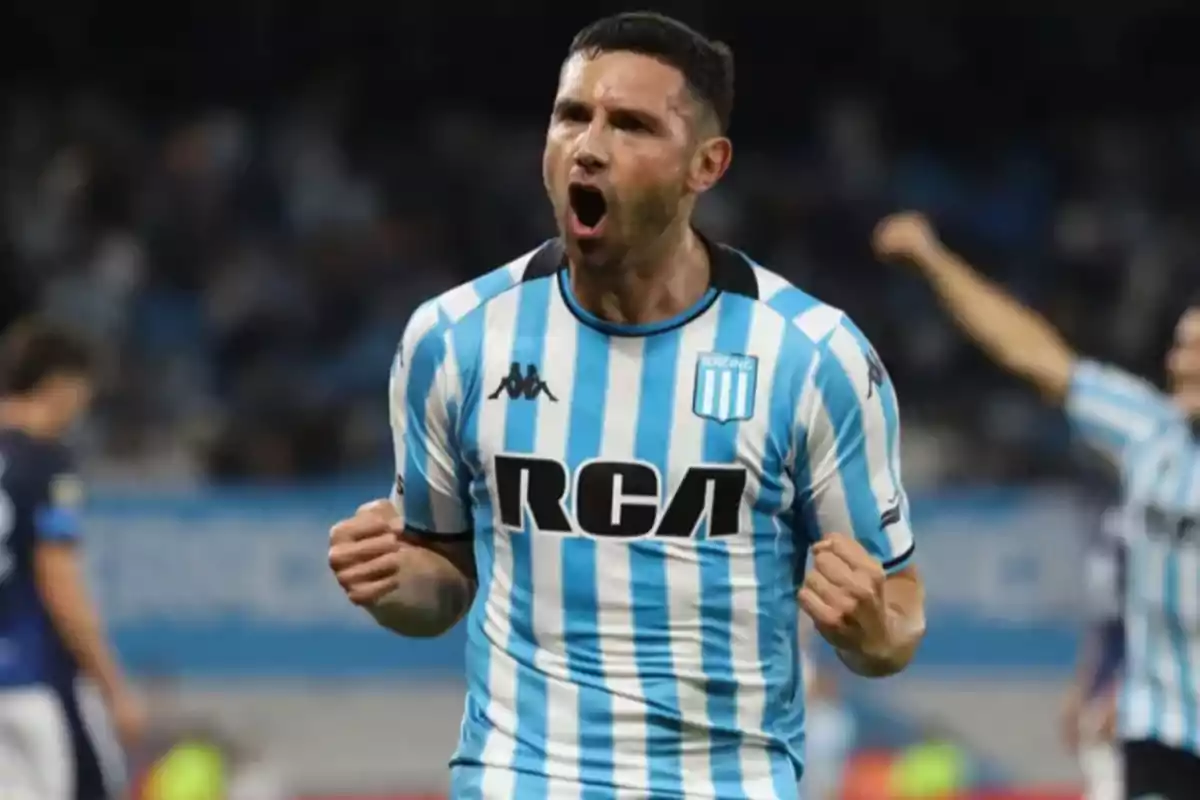 Soccer player in a light blue and white striped uniform celebrating on the field.