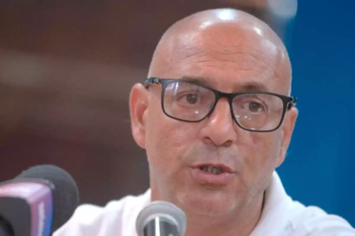 Hombre calvo con gafas hablando frente a un micrófono