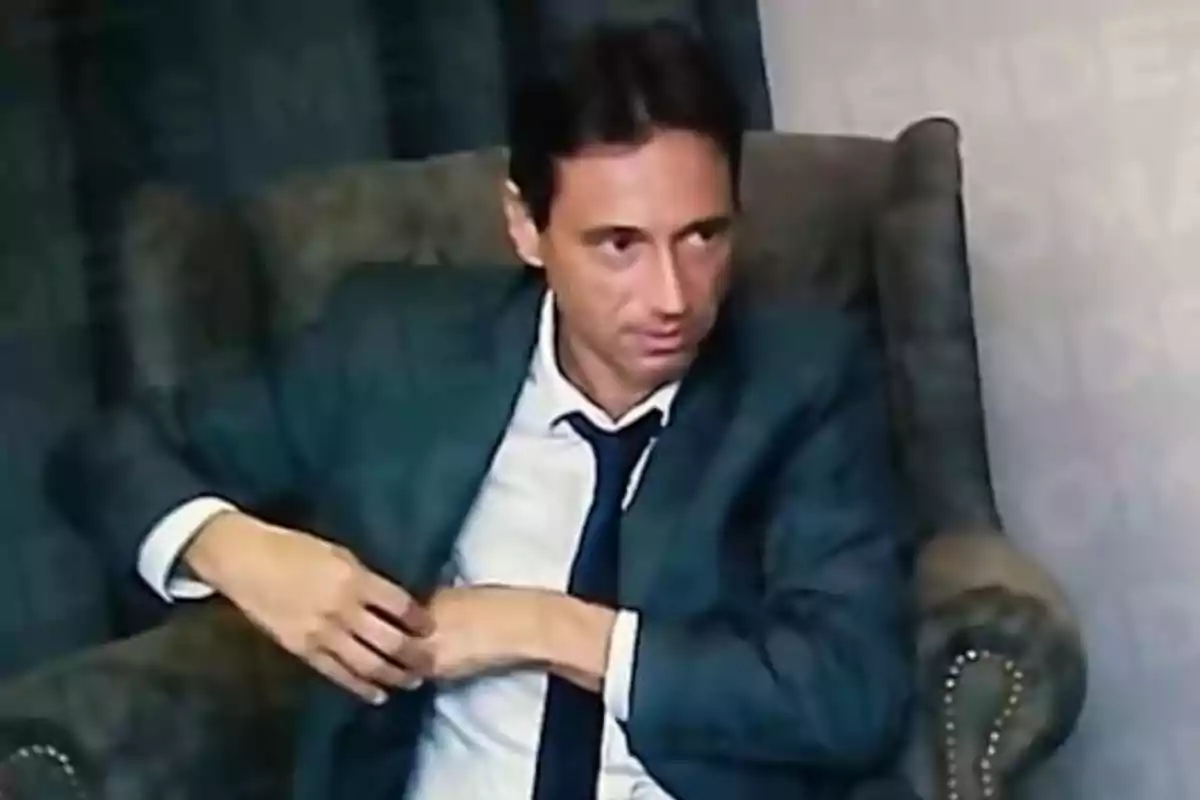 Un hombre con traje y corbata sentado en un sillón, mirando hacia un lado. Un hombre con traje y corbata sentado en un sillón, mirando hacia un lado.