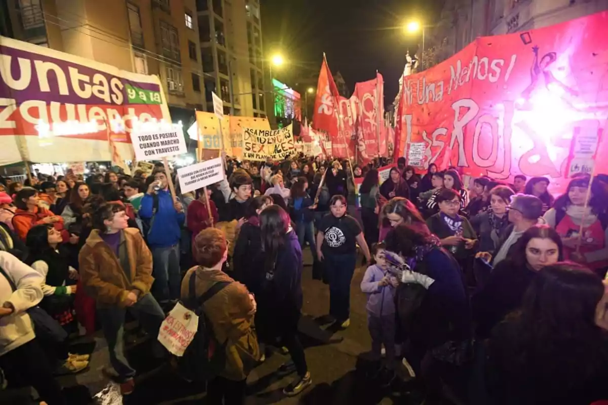 Nighttime demonstration with many people marching down the street, holding colorful banners and flags, in a brightly lit urban setting Nighttime demonstration with many people marching down the street, holding colorful banners and flags, in a brightly lit urban setting
