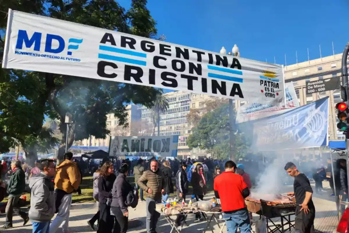 People gathered at an outdoor demonstration with a grill and a large sign that says People gathered at an outdoor demonstration with a grill and a large sign that says